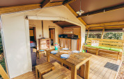 Interior of a safari tent with wooden dining table, kitchen area, and lounge at La Pointe du Talud, France.