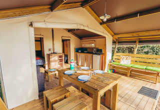 Interieur van een safaritent met houten tafel, keuken en zithoek bij La Pointe du Talud, Frankrijk.