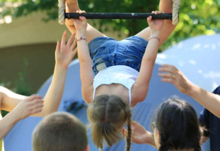 Un bambino penzola a testa in giù da una barra, circondato da adulti pronti ad aiutarlo in campeggio.