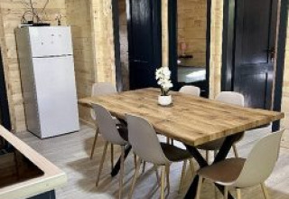 Eethoek in een chalet op camping La Grande Véyière, Frankrijk, met houten tafel, zes stoelen, koelkast en tv.