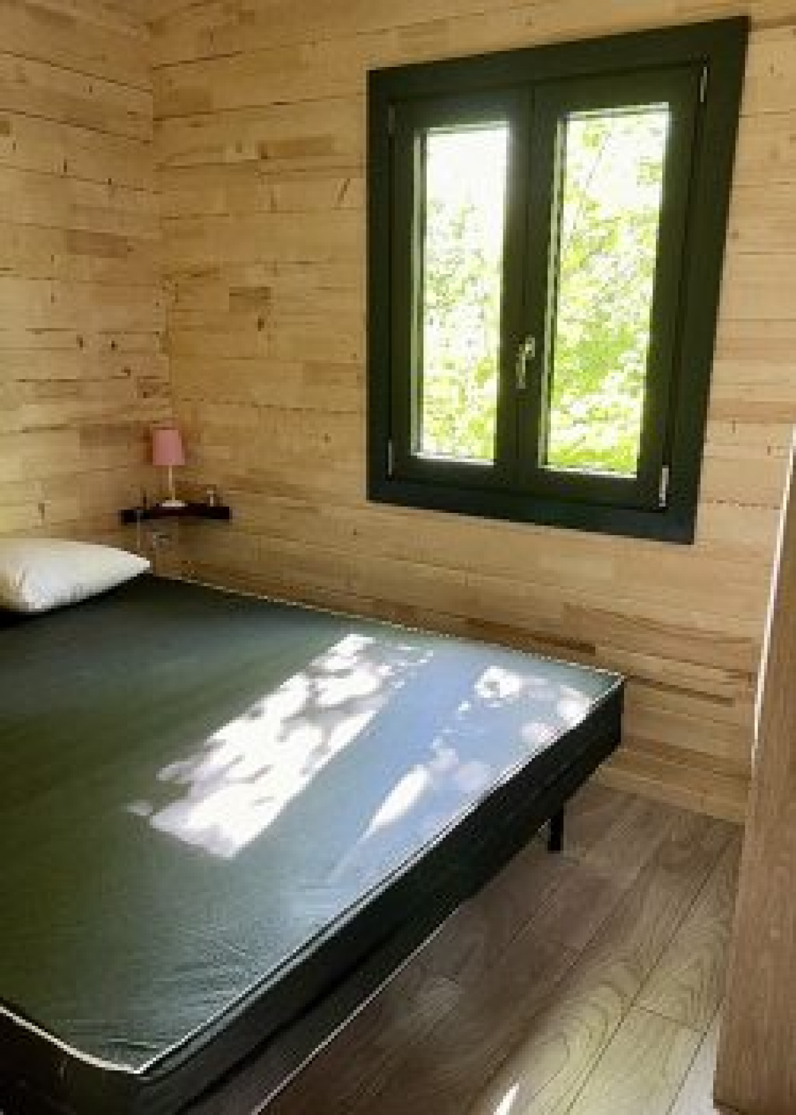 Slaapkamer in het chalet op Camping La Grande Véyière, Frankrijk, met houten muren en een raam met uitzicht.