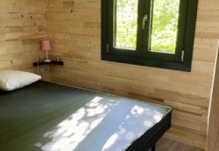 Camera da letto nello chalet al campeggio La Grande Véyière in Francia con pareti di legno e finestra panoramica.