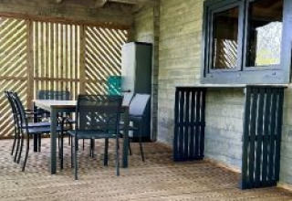 Overdekt houten terras met eettafel en stoelen bij Chalet op Camping La Grande Véyière in Frankrijk.