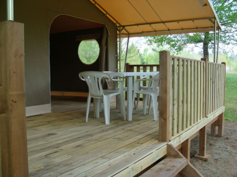 Terrazza in legno con tavolo e sedie di plastica davanti a una tenda safari al Lodge «Canada Classic», Campeggio La Grande Véyière, Francia.