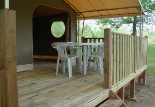 Houten terras met plastieken tafeltje en stoelen voor een safaritent bij Lodge «Canada Classic», Camping La Grande Véyière, Frankrijk.