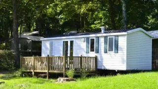 A mobile home called Mobile home Comfort with a wooden deck is set in a green, peaceful woodland area.
