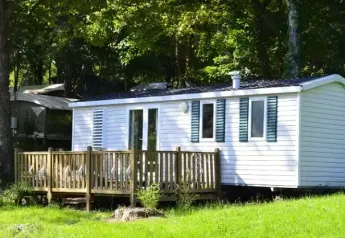 A mobile home called Mobile home Comfort with a wooden deck is set in a green, peaceful woodland area.