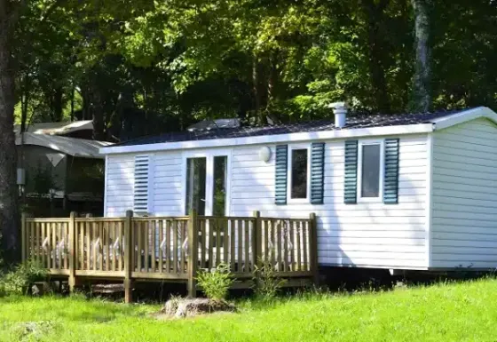 Ein Mobile Home namens Mobile home Comfort mit Holzterrasse steht idyllisch im Grünen am Waldrand.