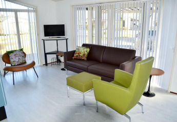 Sala luminosa en la cabaña Comfort 4 personen MIVA de De Woudhoeve con muebles modernos y amplios ventanales.