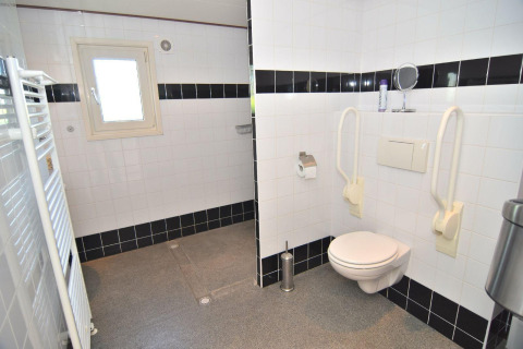 Handicapvenligt badeværelse med væghængt toilet, støttehåndtag og sort-hvide fliser i De Woudhoeve.
