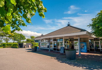 Foto af en moderne kabine under en blå himmel, omgivet af træer og store blomsterkrukker foran indgangen.