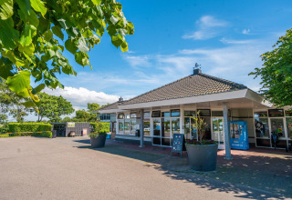 Photo of a contemporary cabin with large windows, surrounded by green trees and flower pots outside.