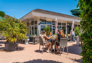 Outdoor dining at a cabin with people enjoying food and drinks, surrounded by plants on a sunny day.