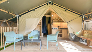 Tenda safari con pavimento in legno, area salotto moderna, angolo cottura e servizi igienici privati.