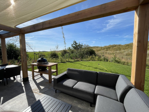 Outdoor terrace at EuroParcs Texel with modern sofa, grill, pergola, and scenic grassy landscape view.