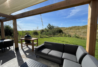 Outdoor terrace at EuroParcs Texel with modern sofa, grill, pergola, and scenic grassy landscape view.