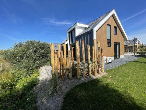 Modern wooden lodge called 'Duinvilla' at EuroParcs Texel, Netherlands, on a sunny day with a clear blue sky.