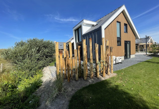 Modern wooden lodge called 'Duinvilla' at EuroParcs Texel, Netherlands, on a sunny day with a clear blue sky.