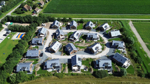 Aerial view of Duinvilla Wellness lodge showing modern cabins in green surroundings and nearby fields.
