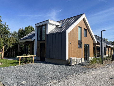Moderno lodge 'Duinvilla' a EuroParcs Texel, Paesi Bassi, con facciata in legno e metallo sotto cielo azzurro.