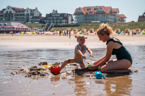 Moeder en dochter bouwen zandkastelen op het strand van Cadzand, Zeeland, met hotels op de achtergrond.