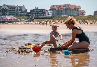 Moeder en dochter bouwen zandkastelen op het strand van Cadzand, Zeeland, met hotels op de achtergrond.