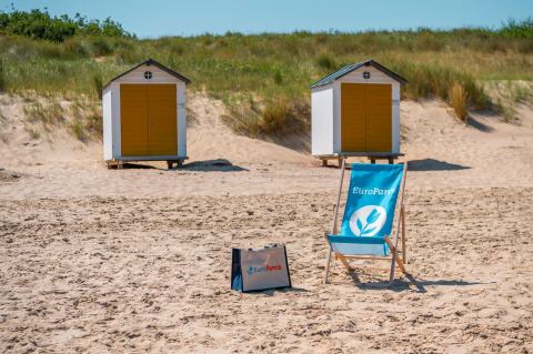 Strand bij Cadzand, Zeeland, met twee gele strandhuisjes en een blauwe EuroParcs strandstoel in het zand.