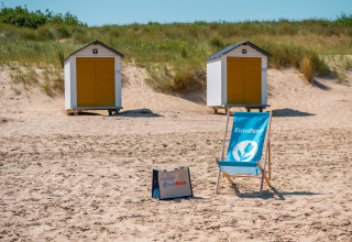 Scena di spiaggia vicino a Cadzand, Zelanda, con due cabine gialle e una sdraio blu EuroParcs sulla sabbia.