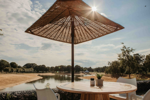 View from Beach Side Scandi showing a lake, beach, parasol, and chairs at Wilsumer Berge, Germany.