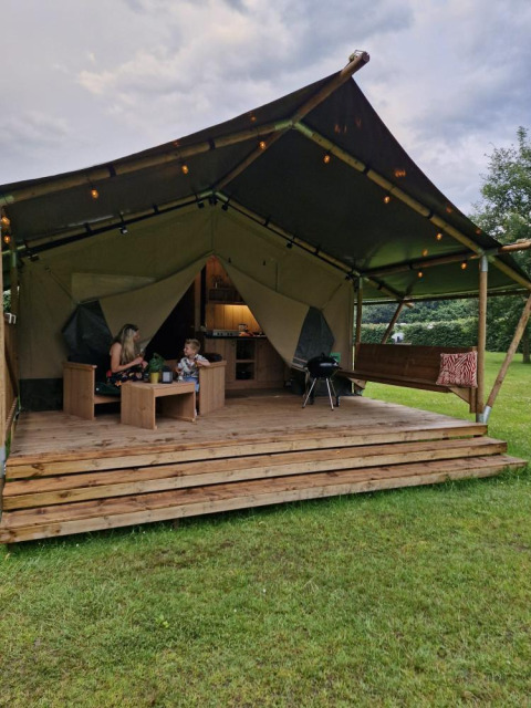 Tente safari Forest Lodge avec sanitaires, deux personnes assises sur la terrasse entourées de verdure.