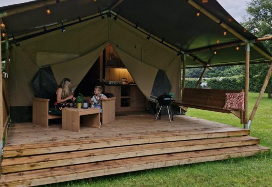 Safaritent Forest Lodge met sanitaire voorzieningen, twee personen op de veranda omringd door natuur.