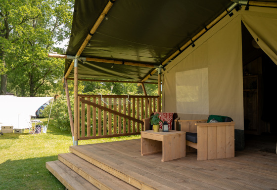Veranda di tenda safari con mobili in legno, terrazza coperta e area verde, servizi inclusi.