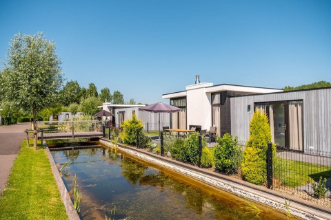 Modern holiday homes by a canal at EuroParcs Bad Meersee holiday park in Zeeland, Netherlands, on a sunny day.