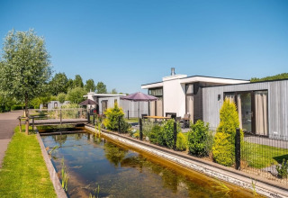 Modern holiday homes by a canal at EuroParcs Bad Meersee holiday park in Zeeland, Netherlands, on a sunny day.