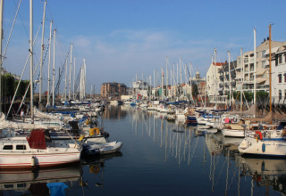 Segelboote und Apartmenthäuser am Hafenkanal nahe Nieuwvliet in Zeeland, Niederlande an einem sonnigen Tag.