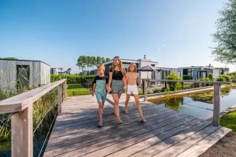 Moeder en twee kinderen wandelen over een houten brug bij EuroParcs Bad Meersee vakantiepark in Zeeland, Nederland.