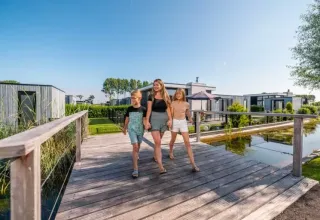 Mutter und zwei Kinder spazieren über eine Holzbrücke im Ferienpark EuroParcs Bad Meersee in Zeeland, Niederlande.