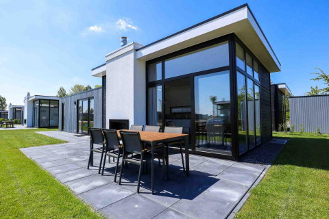 Moderne vakantiewoning met grote ramen en terras bij EuroParcs Bad Meersee in Zeeland, Nederland, zonnige dag.