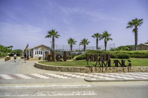 Entrance of Campsite del Mar in Catalonia, Spain, with palm trees, a reception building, and blue sky.