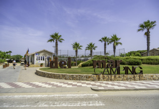 Entrance of Campsite del Mar in Catalonia, Spain, with palm trees, a reception building, and blue sky.