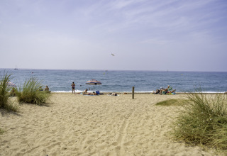 Beach scene at campsite del Mar in Catalonia with people on sand, sea in background, umbrellas and blue sky.