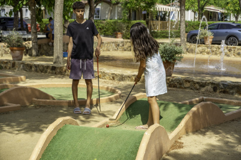 Zwei Kinder spielen Minigolf an einem sonnigen Tag auf dem Campingplatz del Mar in Katalonien, Spanien.