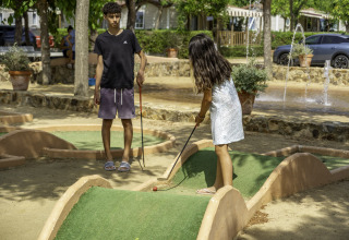 Twee kinderen spelen minigolf op een zonnige dag in Campsite del Mar, een vakantiepark in Catalonië, Spanje.