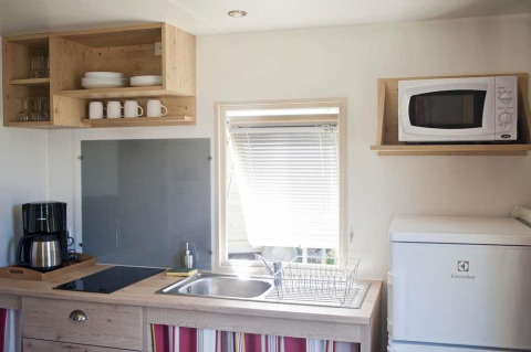 Pequeña cocina en una cabaña con estantes abiertos, microondas, nevera, cafetera y ventana.