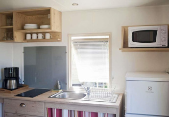 Pequeña cocina en una cabaña con estantes abiertos, microondas, nevera, cafetera y ventana.