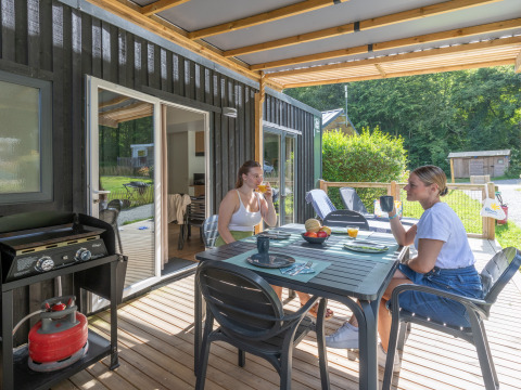 Twee vrouwen genieten van ontbijt op het terras van een Homeflower Premium lodge bij Flower Camping La Chênaie, Frankrijk.