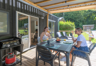 Twee vrouwen genieten van ontbijt op het terras van een Homeflower Premium lodge bij Flower Camping La Chênaie, Frankrijk.