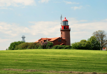 Uitzicht op de rode vuurtoren en lodge 'Am Strand' in Duitsland met groene grasvelden en blauwe lucht.
