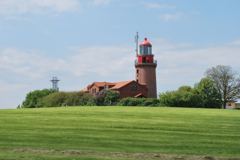 Uitzicht op de rode vuurtoren en lodge 'Am Strand' in Duitsland met groene grasvelden en blauwe lucht.