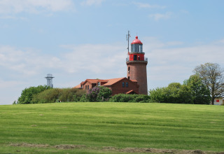 Uitzicht op de rode vuurtoren en lodge 'Am Strand' in Duitsland met groene grasvelden en blauwe lucht.